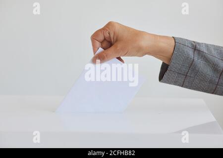Side view close up of female hand putting vote bulletin in ballot box against white background on election day, copy space Stock Photo