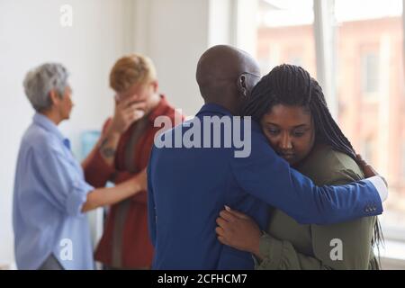 Waist up view at two African-American people embracing during support group meeting, helping each other with stress, anxiety and grief, copy space Stock Photo