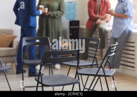 Cropped shot of empty chairs in circle during support group meeting with people chatting in background, copy space Stock Photo