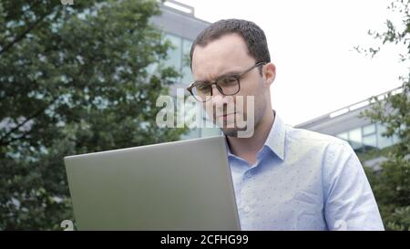 Happy man sitting on bench and using laptop in a park. Stock Photo