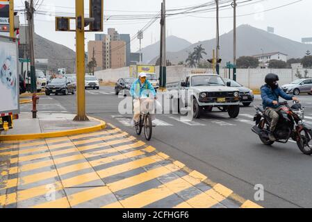 A mature man wearing a protective face mask and riding a bicycle on a busy road In Lima, Perú during the covid-19 pandemia, August 2020. Stock Photo