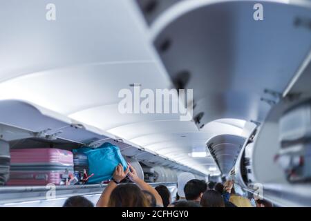man putting luggage on the top shelf on airplane Stock Photo