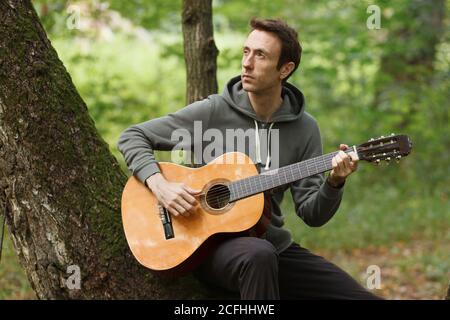 young man plays acoustic guitar on nature in forest Stock Photo