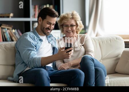 Overjoyed mature woman and adult son using smartphone together Stock Photo