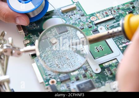 Repairing a printed circuit board with a soldering iron through a magnifying glass. Technology concept. Stock Photo