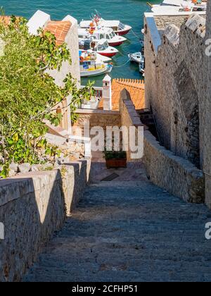 Stairway With a View #2, Hydra island Greece. Walls and steps are made of gray rough stone, but the fig tree foliage and boats swaying in the sea Stock Photo