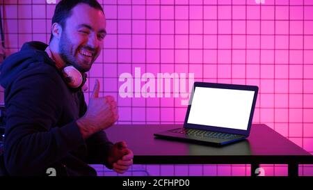 A young cheerful gamer smiling to the camera and looking at laptop. White Display. Stock Photo
