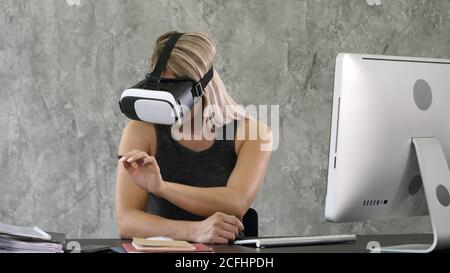 Excited businesswoman wearing virtual reality glasses, happy woman exploring augmented world, interacting with digital interface. Stock Photo