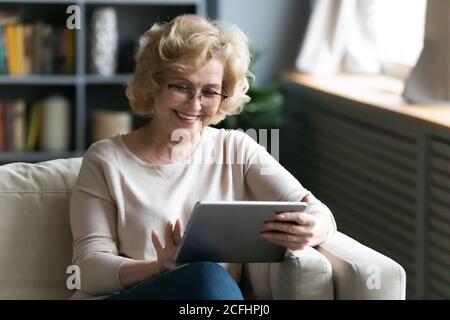 Smiling mature woman wearing glasses using computer tablet at home Stock Photo