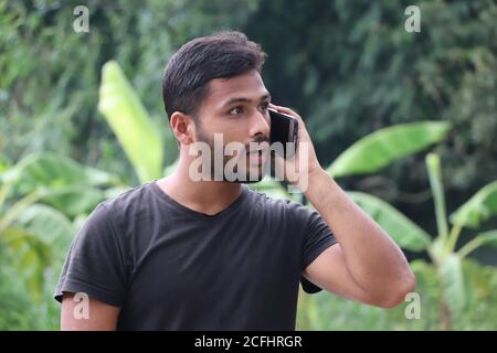 Amazed Asian young man talking on mobile phone, looking surprised Stock Photo