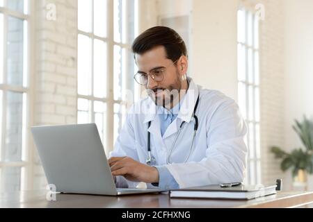 Focused young doctor wearing glasses working on laptop in office Stock Photo