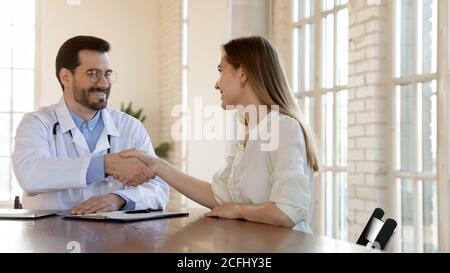 Smiling doctor and young woman shaking hands at meeting Stock Photo