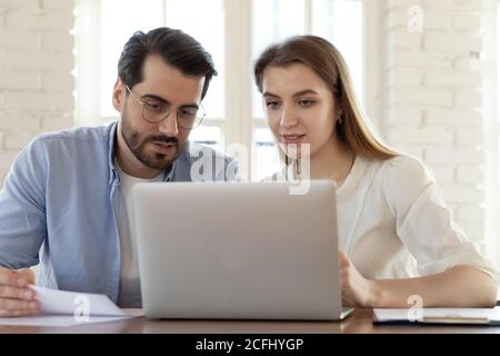 Colleagues working on laptop together, looking at screen, discussing project Stock Photo