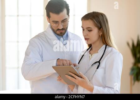 Confident doctor and young nurse talking, working together, using tablet Stock Photo