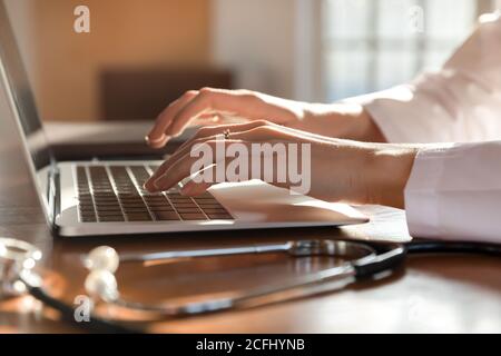 Close up woman doctor working on laptop, typing on keyboard Stock Photo