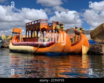 Uros Floating Island on Titicaca Lake, Puno, Peru. View on orange totora boat built in funky style. Ship is decorated with stylized cougar heads.