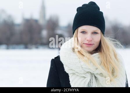 Beautiful young blonde woman wearing a winter outfit in the city snow of Europe. Closeup portrait. Stock Photo