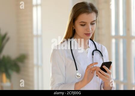 Close up young woman doctor using smartphone, standing in office Stock Photo