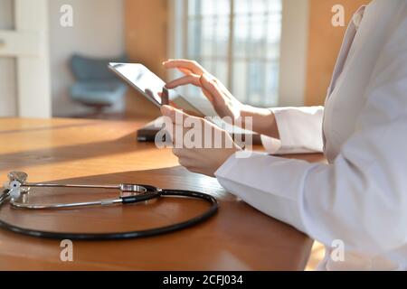 Close up woman doctor holding tablet, sitting at table Stock Photo