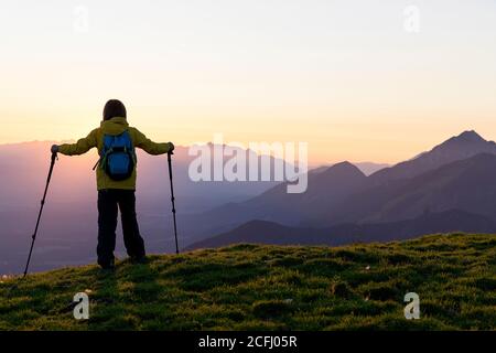 Boy with hiking poles stanidng on top of the mountain at sunset, Krvavec, Slovenia Stock Photo