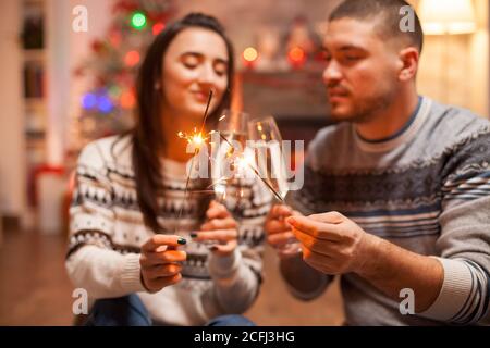 Happy couple clinking glasses of champagne and holding hand fireworks on christmas. Stock Photo