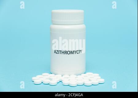 AZITROMYCIN antibiotic in white bottle packaging with scattered pills. Treatments for COVID-19. isolated on blue background. Copy space. Close-up. Stock Photo