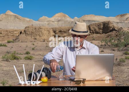 Man pours water into a glass and works outdoors on a laptop at hot summer weather Stock Photo