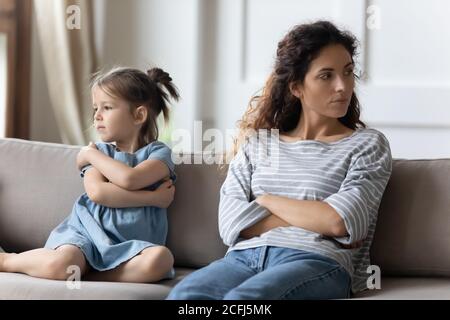 Mother disobedient daughter sit apart on sofa feeling discontent Stock Photo