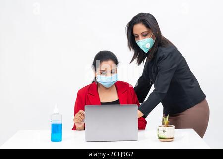 Two professional Indian women working on computer while wearing Covid protection mask, work from home, Corporate employees discussing project Stock Photo