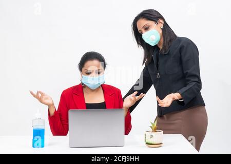 Two professional Indian women working on computer while wearing Covid protection mask, work from home, Corporate employees discussing project Stock Photo
