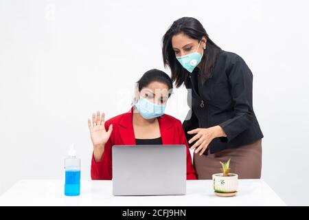 Two professional Indian women working on computer while wearing Covid protection mask, work from home, Corporate employees discussing project Stock Photo