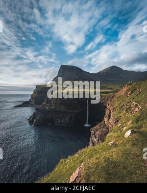 Gasadalur village and Mulafossur its iconic waterfall during summer with bluw sky. Vagar, Faroe Islands, Denmark. Rough see in the north atlantic