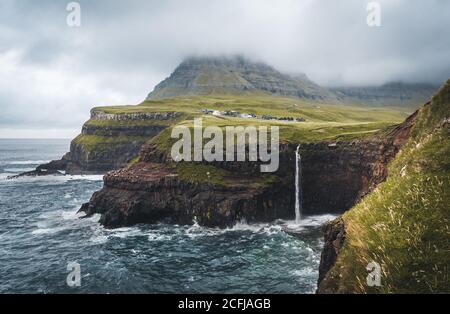 Gasadalur village and Mulafossur its iconic waterfall, Vagar, Faroe Islands, Denmark. Rough see in the north atlantic ocean. Lush greens during summer Stock Photo