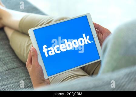 Woman Hands using iPad with Facebook homepage on screen. Facebook the biggest social network website. Stock Photo