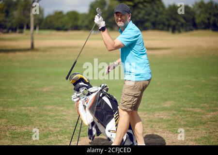 Middle-aged man playing a round of golf on a golf course turning to smile at the camera as he selects a club from his bag for the next shot
