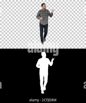 Young confident man in shirt and jeans walking towards camera and pointing to the sides, Alpha Channel Stock Photo