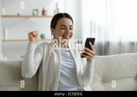 Overjoyed young smiling woman celebrating receiving good news notification. Stock Photo
