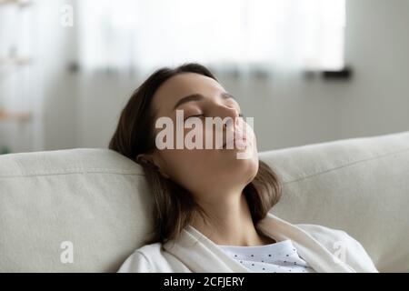 Head shot tired millennial woman leaning on cozy couch. Stock Photo