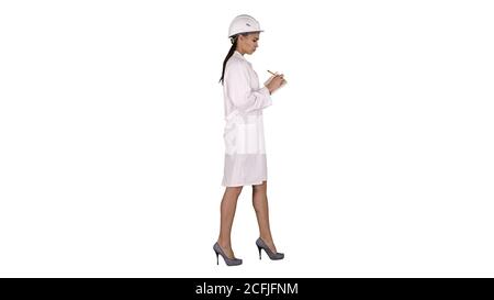 Woman engineer with helmet is holding pen and checklist putting something down while walking on white background. Stock Photo