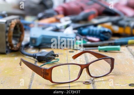 Workshop desktop of electrician repairman with his eyeglass. The eyeglasses on a table full of tools and components for repairing electrical appliance Stock Photo