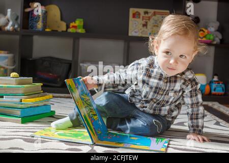 Happy sweet baby boy reading books sitting on the floor, at home Stock Photo