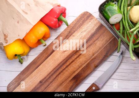 Yellow orange and red capsicum with chopping board on table  Stock Photo