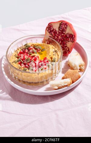 Pumpkin hummus dip with pomegranate and seed topping on pink textile background. Healthy Thanksgiving vegetarian appetizer Stock Photo