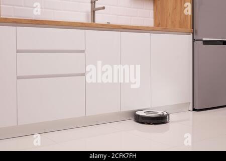 Robot vacuum cleaner on a tiled kitchen floor Stock Photo