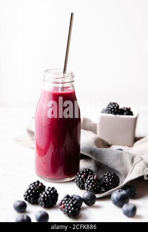 Front shot of a glass bottle with berry smoothie, with a metal straw in it. Vertical image. Stock Photo