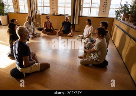 Group of diverse people with instructor sitting on floor and practicing meditation during traditional chi kung session in studio Stock Photo