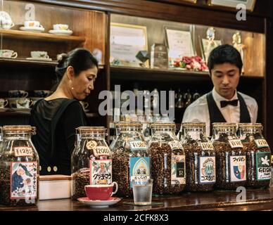 Dazaifu, Fukuoka, Japan - Roasted coffee beans from all over the world. Glass jars displayed on a coffee bar table. Baristas preparing coffee. Stock Photo