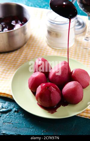 From above of anonymous person at table with sweet poached pears in red wine in plate placed in kitchen Stock Photo