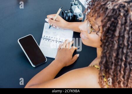 From above Woman sitting at table in cafe and working remotely while writing in notepad Stock Photo