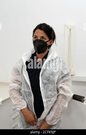 Female medical specialist putting on protective suit with face mask while preparing for work during coronavirus pandemic Stock Photo